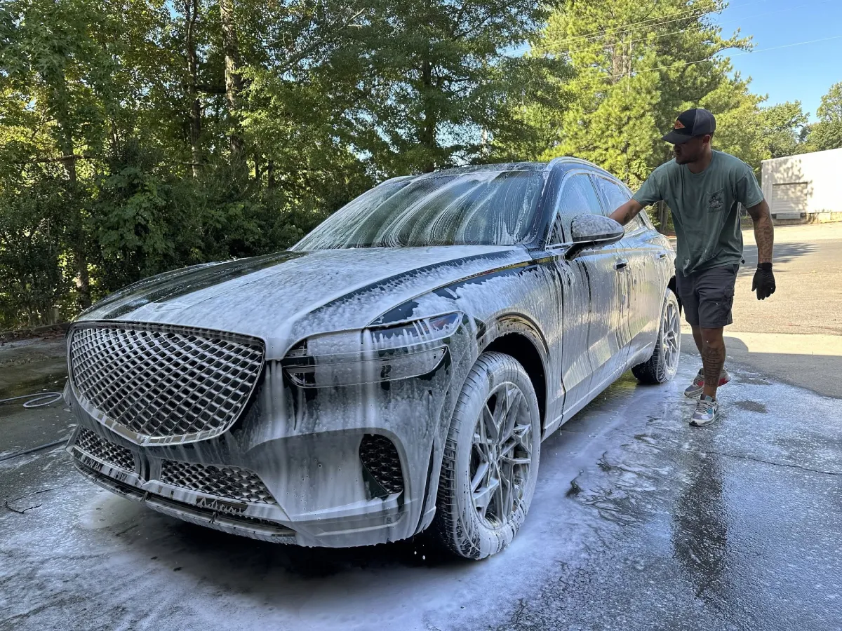 Man hand washing a soapy Genesis SUV outdoors during a mobile detailing service.