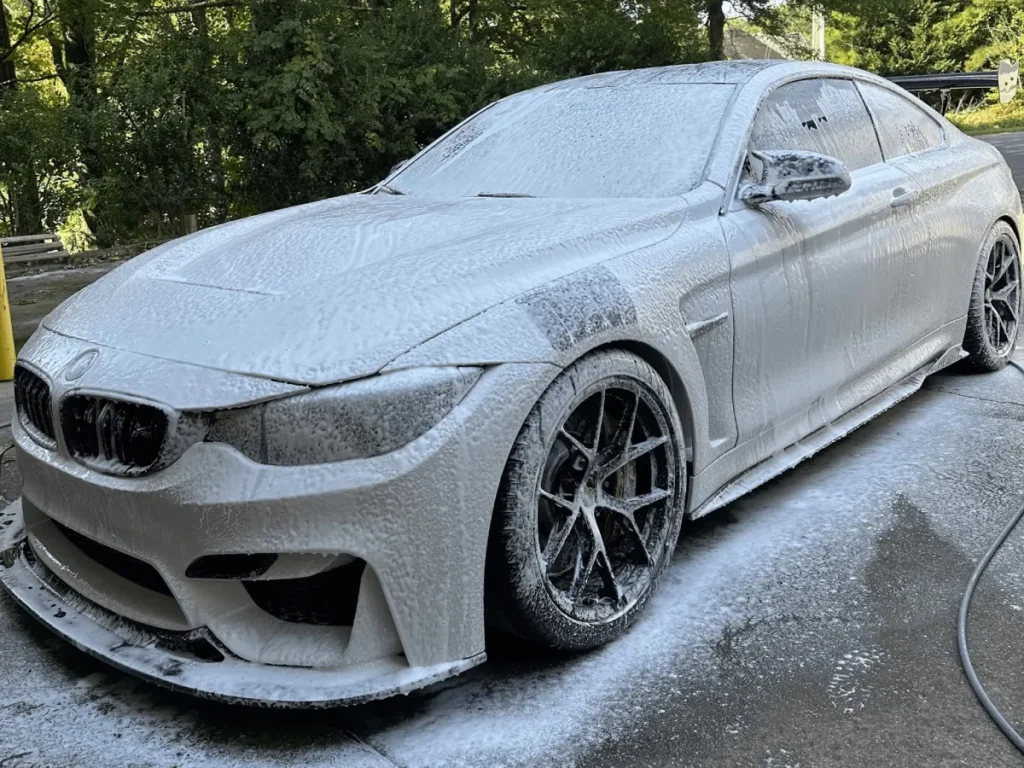 BMW coupe completely covered in thick soap foam during a mobile detailing hand wash.